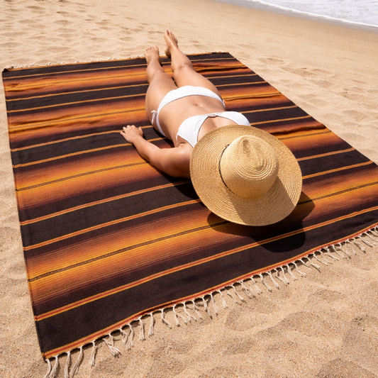 Person lying on a striped blanket towel with a straw hat, ocean in the background