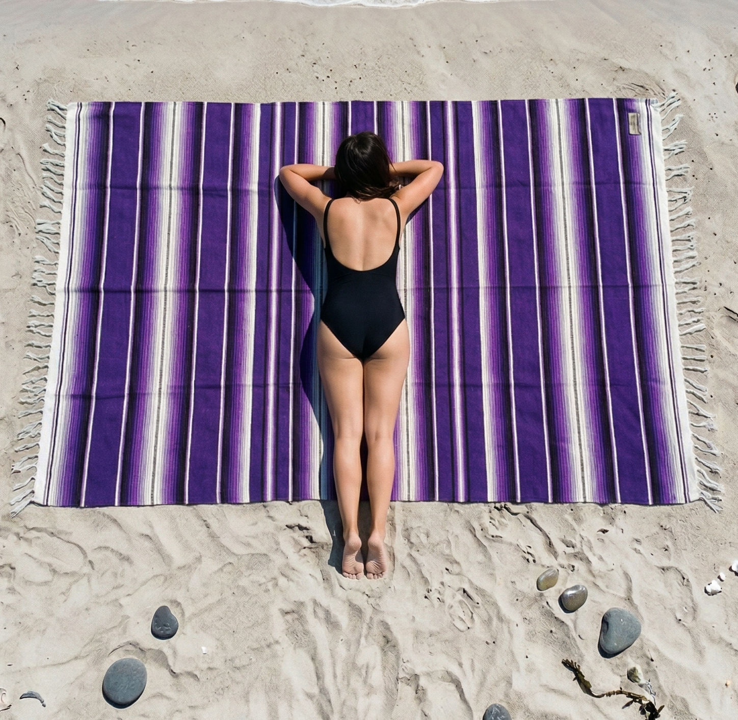 Person lying on a purple striped beach towel at the beach