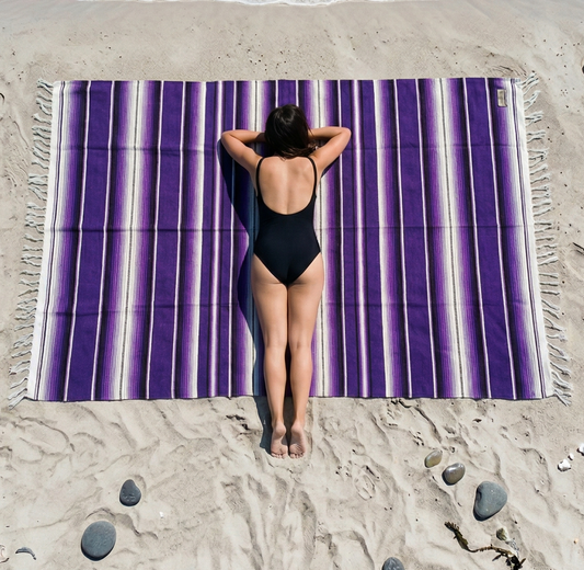 Person lying on a purple striped beach towel at the beach