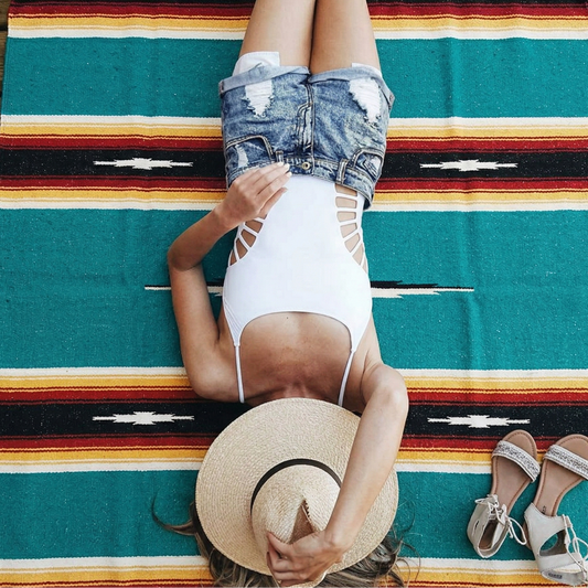Person lying on a colorful striped rug with a straw hat and sandals nearby